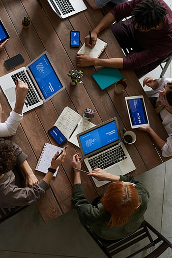people sitting, wooden table, diverse group, professionals brainstorming, laptops, notepads, modern office, discussion outline, collaborative work, office meeting, team collaboration