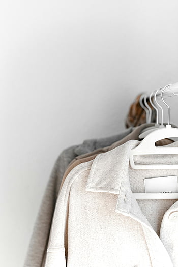 Neutrale Kleidung, weiße Kleiderbügel, Kleiderständer, einfache Kulisse, ordentlich aufgehängt, neutrale Töne, minimalistischer Stil, Garderobenorganisation, Modefotografie, Kleidungsdisplay, Hängende Kleidungsstücke