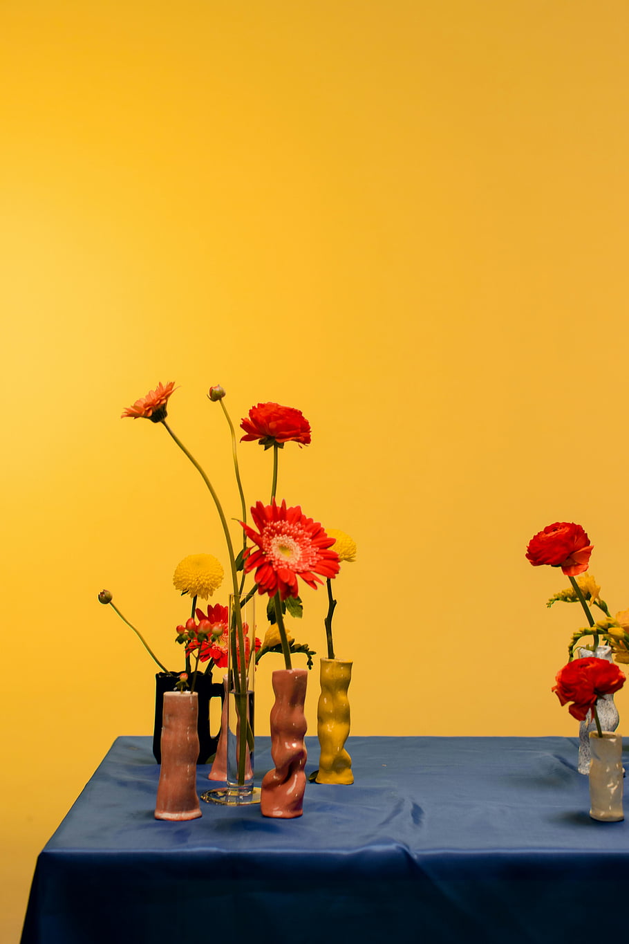 orange flowers, ceramic vases, table arrangement, colorful flowers, unique vases, bold yellow background, floral arrangement, striking flowers, decorative vases, vibrant colors, table decor