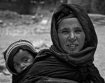 fotografie ve stupních šedi, Žena v černém hidžábu, nesoucí dítě, pletené čepice, černobílý portrét, matka a dítě, Rodinné pouta, marocký, kulturní dědictví, tradiční oděv, Emocionální spojení