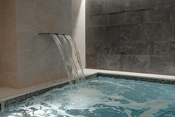 indoor pool, cascading waterfall, marble walls, luxury spa, serene experience, spa experience, indoor spa, waterfall feature, spa design, spa pool, spa waterfall