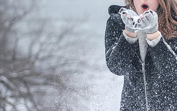 Women's Black Zip Up Hooded Jacket, cozy winter clothing, blowing snowflakes, snowy setting, outdoor winter scene, winter fashion, snow-covered trees, winter gloves, excited woman, winter jacket, outdoor winter activity