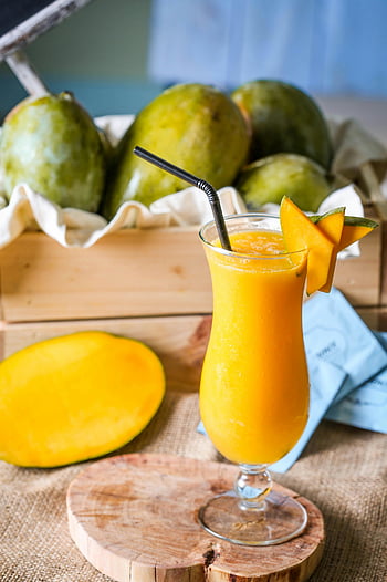 Mango mehu, kirkas juomalasi, keltainen mehu, kesäjuoma, virkistävä juoma, mangoviipaleet, koristeltu juoma, trooppinen hedelmä, mangokoriste, puinen tarjotin, olki