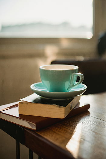コーヒーカップ、 積み上げ書籍、 太陽に照らされた窓、 居心地の良い設定、 温かい飲み物、 穏やかな雰囲気、 木製テーブル、 屋内シーン、 隅を読む、 朝の光