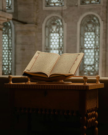 open Koran, wooden table, mosque interior, spiritual ambiance, decorative stand, Islamic scripture, religious text, Quran reading, sacred book, Islamic art, mosque decor