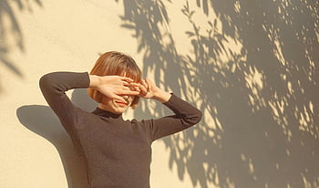 woman, black sweater, outdoor, bright day, stylish, covering eyes, sunlight, shadow, wall, casual, fashion