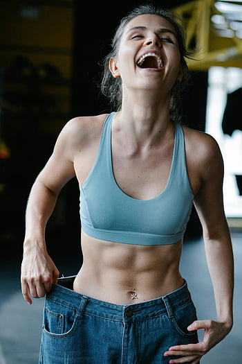 Fit Frau, lächelnd, Gewichtsverlust, übergroße Jeans, Fitnessstudio, Fitness, gesunder Lebensstil, Körper positiv, trainieren, Erfolg, Glück