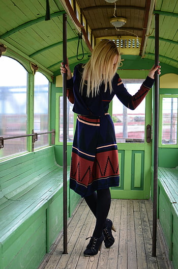 woman, vintage train car, contemporary fashion, retro aesthetics, stylish outfit, green interior, blonde hair, high heels, wooden floor, vibrant colors, posing inside