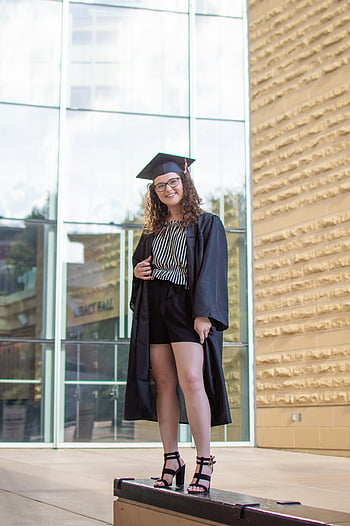 in graduation gown, confident female graduate, cap and gown, celebrating outdoors, graduation photo, outdoor graduation, female graduate, graduation celebration, graduation day, graduation portrait, graduation ceremony