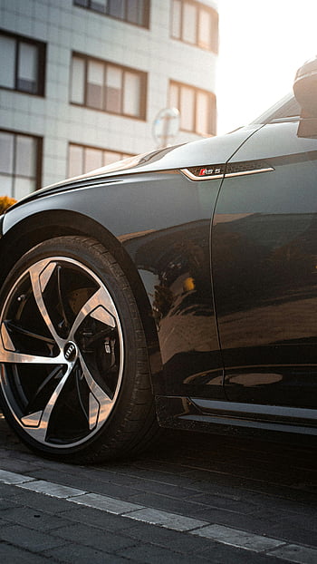 modern sport car wheel, close-up view, automotive design, urban backdrop, sunlight reflection, car wheel, modern car, sport car, urban setting, car design, wheel design