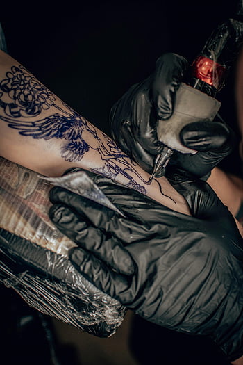 tattoo artist, intricate designs, arm tattoo, close-up shot, tattoo process, tattooing, black gloves, tattoo machine, detailed tattoo, skin art, tattoo studio