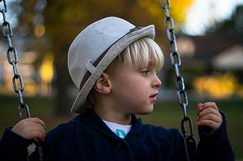 Kind im grauen runden Hut, Hängende Schaukel, kleiner Junge, Spielplatz Schaukel, draußen, Herbst, friedlicher Moment, Spielplatz, Herbstsaison, Spielen im Freien, Kind im Hut