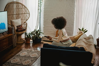 Ethnische Frau, Fernbedienung, Fernsehen, gemütliches Wohnzimmer, Styles Wohnzimmer, junge Frau, Sofa, Zuhause, fokussiert, ethnisch, Fernseher
