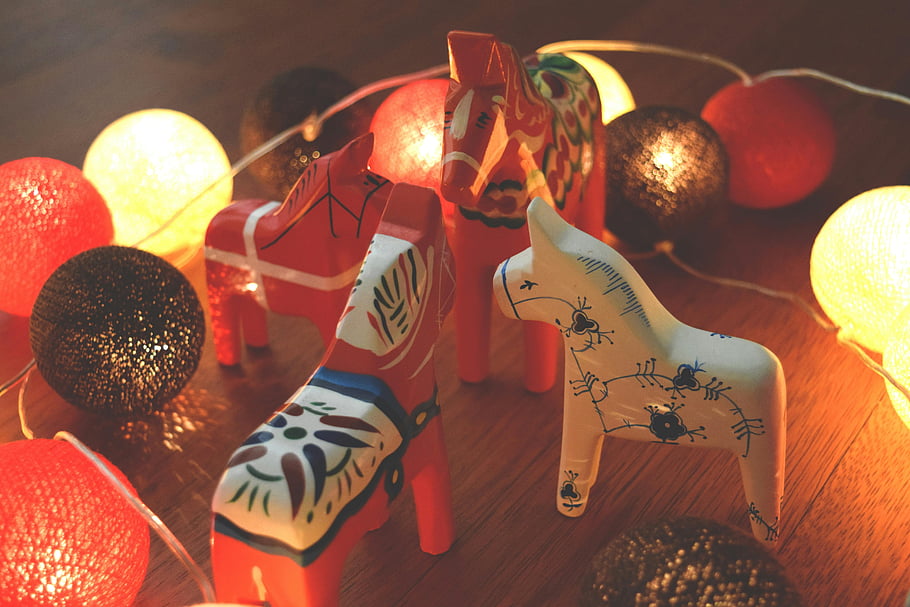 wooden horse figurines, assorted-color horses, decorative horse toys, colorful horse statues, festive lighting, wooden horse collection, hand-painted horses, indoor decoration, holiday decor, traditional horse figurines, ornamental horses