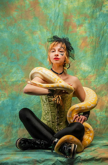 woman with snake, python, bold makeup, corset, stylish woman, snake on shoulders, green background, black leggings, black boots, veiled woman, artistic portrait