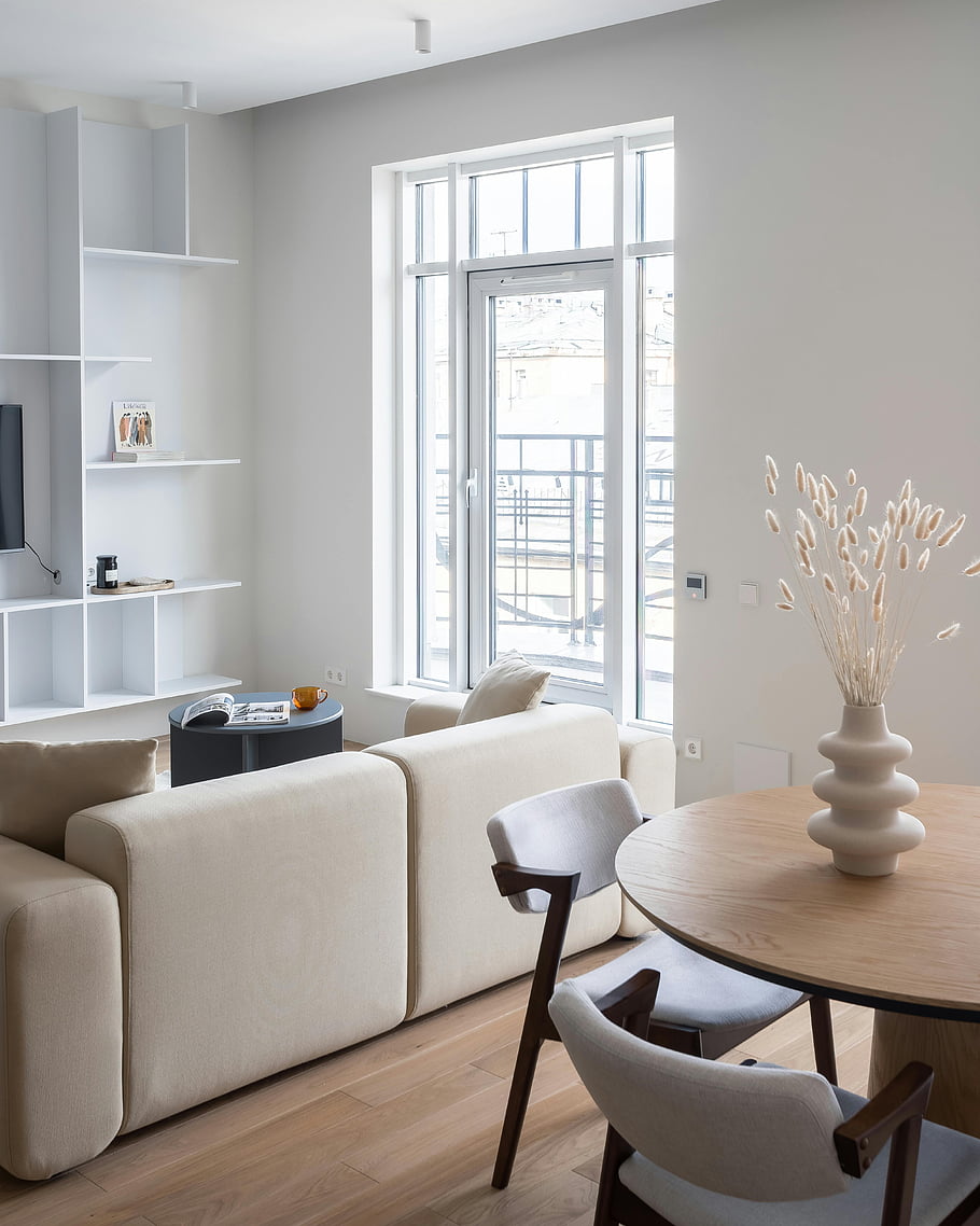 Zjednodušující obývací pokoj, neutrální barvy, minimalistický design, moderní nábytek, přirozené světlo, Petrohrad, Světlý interiér, moderní dekor, Otevřené regály, dřevěné podlahy, kulatý stůl