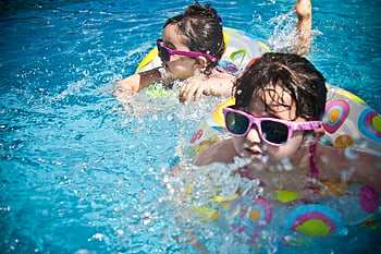 girls swimming, daytime swimming, pool activity, children in water, sunglasses, inflatable rings, summer fun, water play, outdoor recreation, kids in pool, splashing water