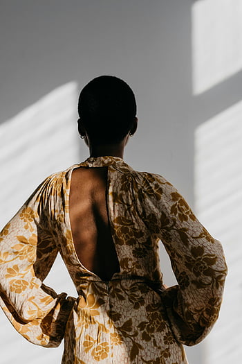 black lady, fashionable dress, white wall, elegant back view, stylish floral dress, indoor portrait, artistic lighting, backless dress, indoor fashion, elegant woman, stylish outfit