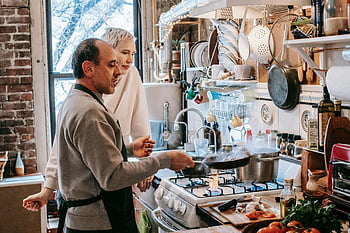 cozy kitchen, couple cooking, homemade cuisine, frying pan, man preparing, wife assisting, kitchen atmosphere, cooking together, kitchen tools, food preparation, gas stove