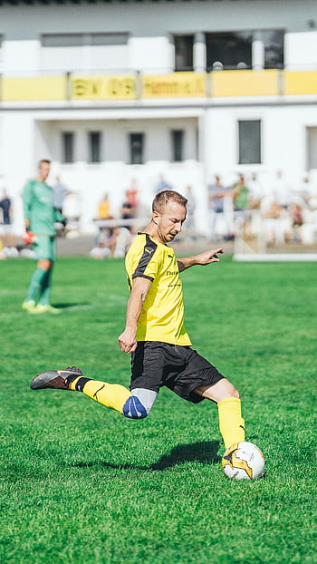 soccer player, yellow jersey, kicking ball, green field, sunny day, outdoor match, selective focus, football, sports action, athletic performance, sports photography