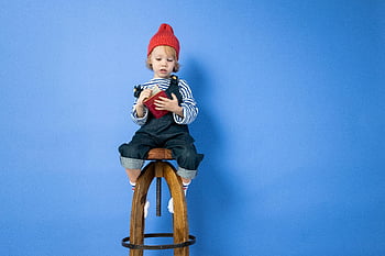 cute child, red hat, reading, wooden stool, blue background, boy, striped shirt, brown wooden seat, long sleeve shirt, sitting, book