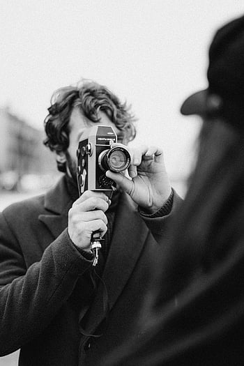 Mand i sort jakke, holde kameraet, vintage kamera, sort og hvidt foto, udendørs fotografering, mand tager foto, retro kamera, gadefotografering, sort jakke, udendørs scene, vintage fotografering