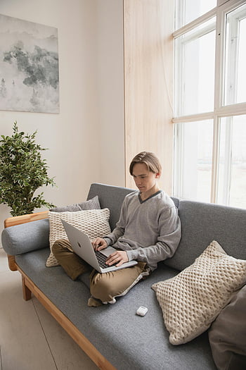 Muž sedí na gauči, laptop, Útulná pohovka, Světlý obývací pokoj, mladý muž, pomocí přenosného počítače, Vnitřní nastavení, pohodlné nastavení, domácí kancelář, Příležitostná práce, moderní obývací pokoj