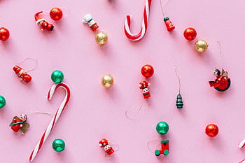 theme decoration, pink surface, Christmas ornaments, candy canes, playful arrangement, festive decor, holiday theme, red and white, gold ornaments, Christmas candy canes, flat lay photography