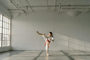 Dívka praktikující taekwondo, Mladý bojový umělec, Představení kopu, Vnitřní studio, přirozené osvětlení, Bílý gi, červený pás, Výcvik bojových umění, Studio praxe, ženský bojový umělec, Taekwondo kop