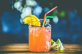 Letní citrusový koktejl, mason jar, plátky citronu, brčka, osvěžující nápoj, růžová tekutina, sklenka, ledové kostky, venkovní nastavení, dřevěný stůl, květiny