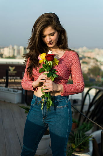 woman in red and white striped top, holding roses, young woman, denim, bouquet of roses, sunny day, outdoor, rooftop, cityscape, casual outfit, flowers