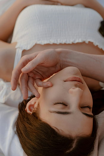 リラックスした若い女性、 屋外に横たわっています、 手を顔に、 目を閉じて、 平穏な瞬間、 ホワイトトップ、 自然な設定、 穏やかな雰囲気、 屋外リラクゼーション、 静かな情景、 穏やかな表情