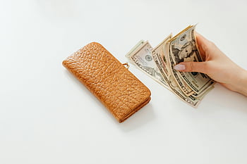 osoba drží peníze, bílý stůl, hnědá kožená peněženka, Americké dolarové bankovky, Počítání peněz, bílý povrch, peněženka vedle peněz, finanční plánování, Manipulace s hotovostí, osobní finance