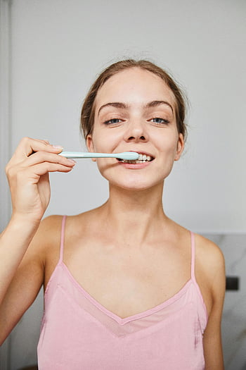 woman brushing teeth, pink pajamas, oral hygiene, toothbrush, indoors, dental care, morning routine, personal care, healthy teeth, woman in pajamas, bathroom hygiene