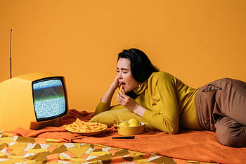 Donna con camicia gialla, guardare la TV, Mangiare snack, tv vintage, impostazione retrò, sfondo colorato, sdraiarsi, pranzo informale, Scena indoor, merenda, visione televisiva