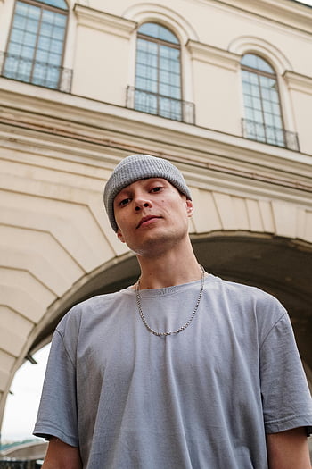 Mann in Grau, Graues Crew -Halshemd, graue Strickkappe, Freizeitkleidung, Historischer Stadtbogen, selbstbewusste Pose, urbane Mode, Streetstyle, junger Mann, Porträt im Freien, Stadtbild Hintergrund