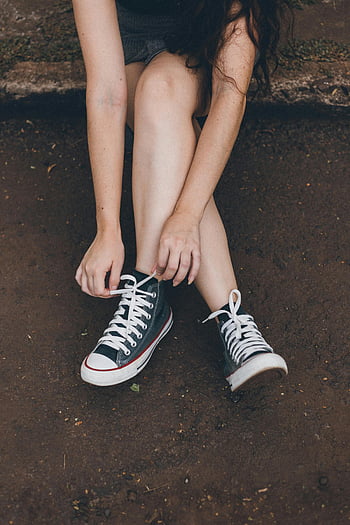 donna che lega i lacci delle scarpe, scarpe da ginnastica converse, stile esterno casual, terra sporca, Conversa classica, Scarpe allacciate, seduto a terra, moda all'aperto, Stile casual, lacci delle scarpe, scarpe da ginnastica