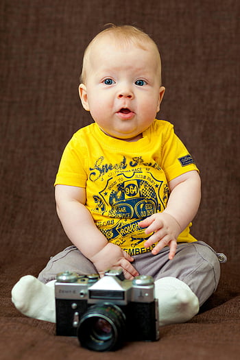babyjongen, geel T-shirt, grijze bodem, klassieke camera, studiofoto, charmante baby, heldere kleding, zittende baby, studio portret, baby fotografie, vintage camera