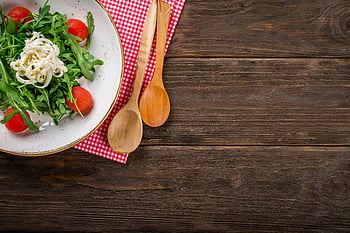 arugula salad, tomatoes, cheese, rustic wooden table, healthy dining, vibrant salad, wooden spoons, checkered napkin, fresh vegetables, plate of salad, healthy meal