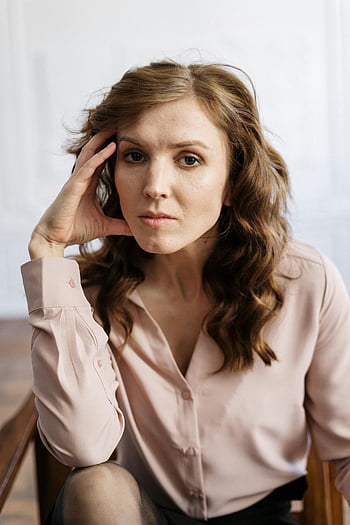woman, white button up shirt, holding hair, curly hair, thoughtful expression, sitting indoors, portrait, casual pose, indoor setting, natural light, professional look