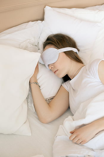 woman sleeping, sleep mask, cozy bed, white sleep mask, serene scene, comfortable sleep, restful sleep, bedroom, pillow, white bedding, relaxation
