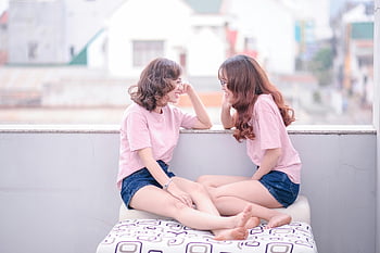 pink t-shirts, young women, casual attire, relaxed moment, balcony, sitting, two women, outdoor setting, friendship, casual clothing, pink shirts