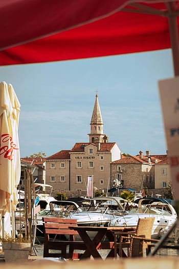 Προκυμαία Budva, ελλιμενισμένα σκάφη, ιστορική αρχιτεκτονική, ηλιόλουστη μέρα, εστιατόριο Waterfront, γραφική θέα, Βούδβα λιμάνι, υπαίθρια τραπεζαρία, παραθαλάσσια τοπία, Διαδρομές του Μαυροβουνίου, παραθαλάσσια πόλη
