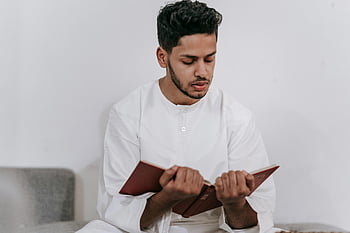 Persona che tiene in mano il Corano, giovanotto, Abbigliamento islamico, leggere il Corano, in casa, studio religioso, pratica spirituale, uomo musulmano, libro religioso, Lettura intima, abbigliamento bianco