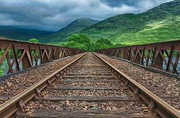 Brown Train Rail Way, rusty railway tracks, iron bridge, Stirling Scotland, lush green mountains, dramatic clouds, railway scenery, scenic train tracks, historic railway, natural landscape, overcast sky