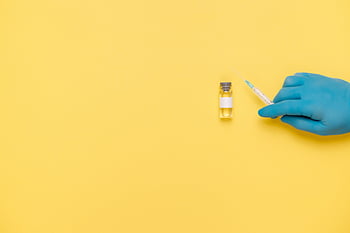 blue gloves, syringe, vaccine vial, yellow backdrop, medical equipment, healthcare, injection, blue gloved hand, medical procedure, vaccination, yellow background