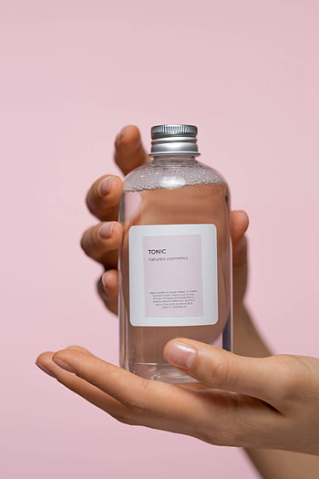 Tonik pielęgnacji skóry, szklana butelka, trzymając się za ręce, różowe tło, Zbliżenie estetyczne, Naturals Kosmetics, Produkt kosmetyczny, produkt do pielęgnacji skóry, butelka kosmetyczna, minimalistyczny design, Butelka tonera