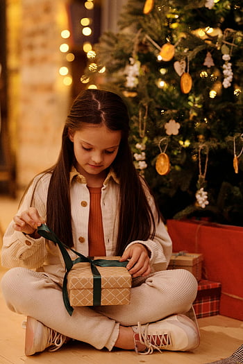 hadiah Natal, gadis muda, pohon dihiasi, Hadiah pembukaan, Adegan yang meriah, semangat liburan, pohon Natal, momen yang menggembirakan, pembungkus kado, Perayaan Liburan, dekorasi Natal