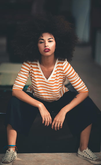 žena sedící, Oranžová a bílá pruhovaná košile, košile s výstřihem, lokevy rukávy, účes Afro, Příležitostný elegantní oděv, Módní portrét, stylová žena, černá sukně, tenisky, Vnitřní nastavení