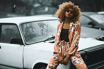ruskea kukkatuloste, kukkapuku, vintage-tyyliin, klassinen auto, muodikas nainen, luottavainen asento, aurinkolasit, afro hairstyle, ulkona, auton valokuvaus, retro-muoti